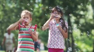 孩子们在夏天的公园里玩。 两个小女朋友做肥皂泡和微笑。 姐姐和妹妹